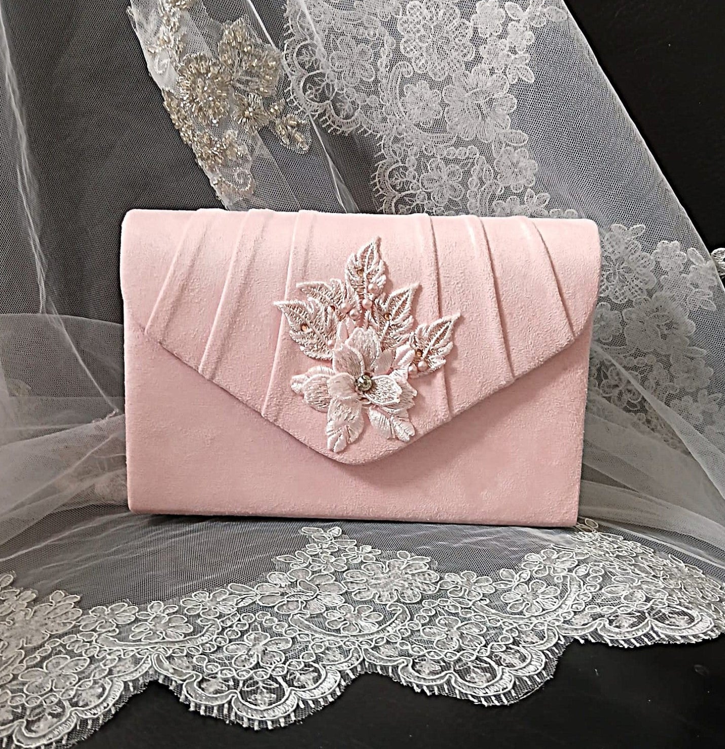 A light pink velvet clutch bag with pleated detailing and a large 3D floral embellishment on the front flap