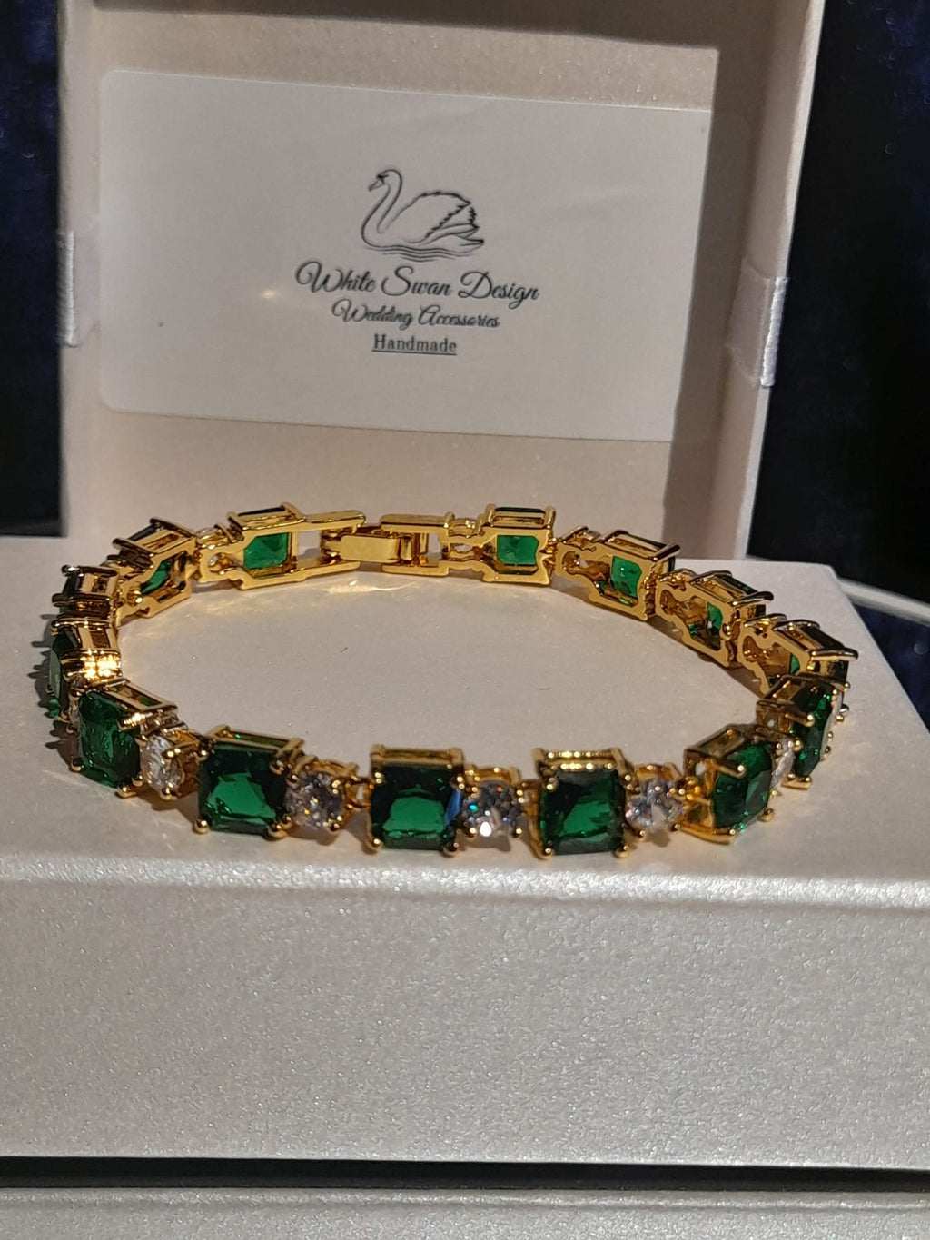Gold bracelet with green gemstones on a branded box