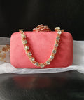 Coral red clutch bag with gold chain handle on a black background