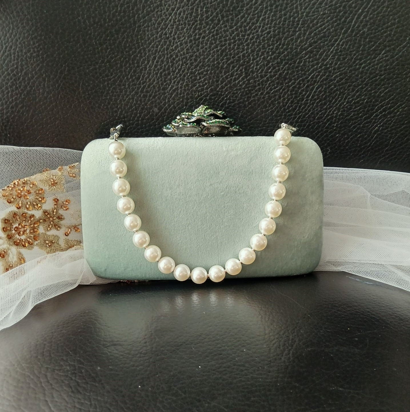 Sage green clutch with a pearl handle on a dark surface.