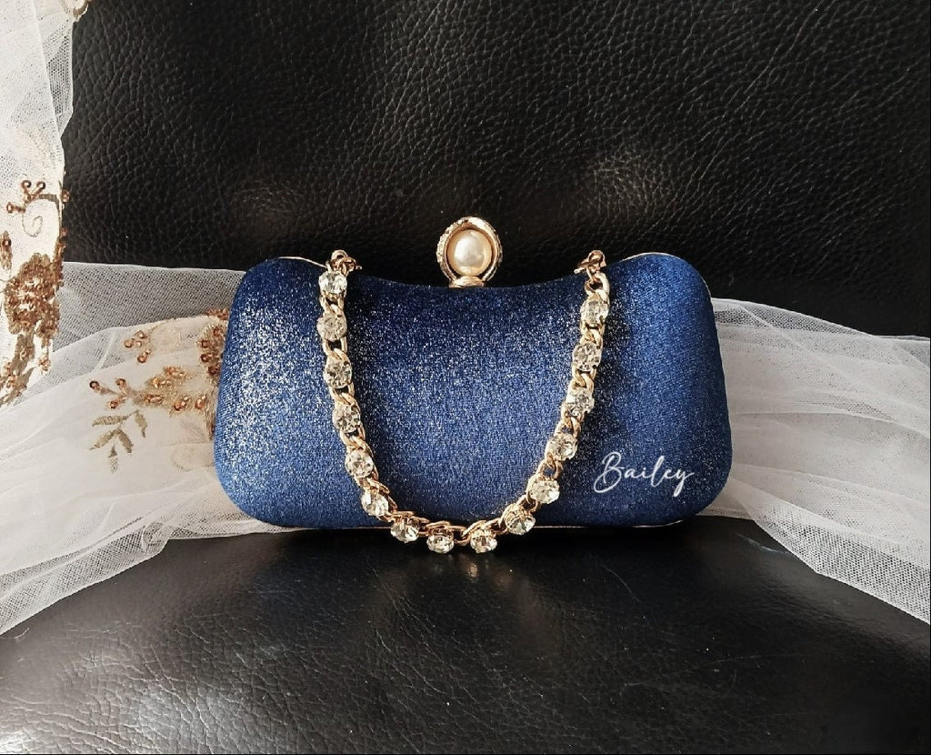 Blue glittery clutch with a gold crystal chain handle on a black surface.