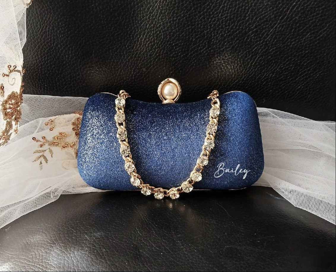 Blue glittery clutch with a gold crystal chain handle on a black surface.