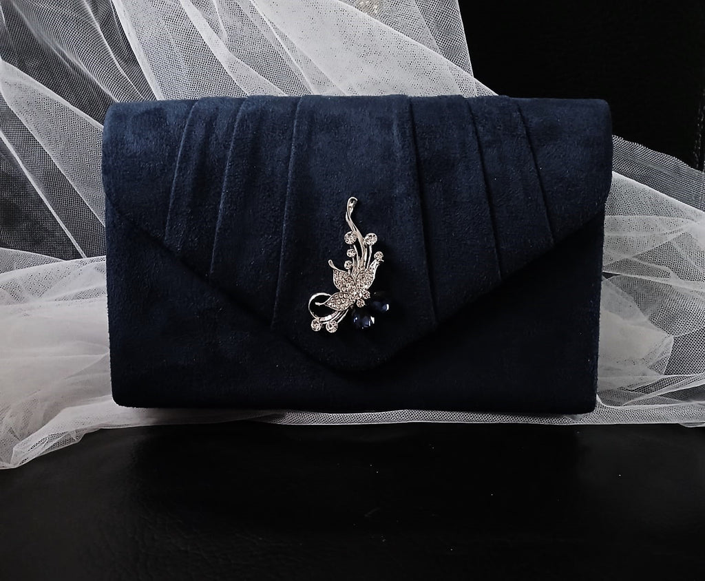 Navy blue clutch bag with decorative brooch on a white fabric background