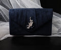 Navy blue clutch bag with decorative brooch on a white fabric background