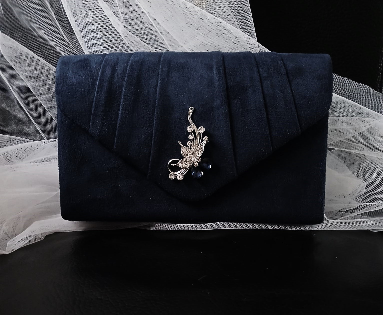 Navy blue clutch bag with decorative brooch on a white fabric background