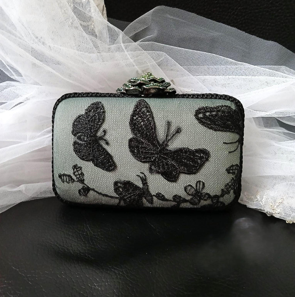 sage green with Black butterfly lace clutch bag on a dark surface with white fabric in the background