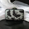 sage green with Black butterfly lace clutch bag on a dark surface with white fabric in the background