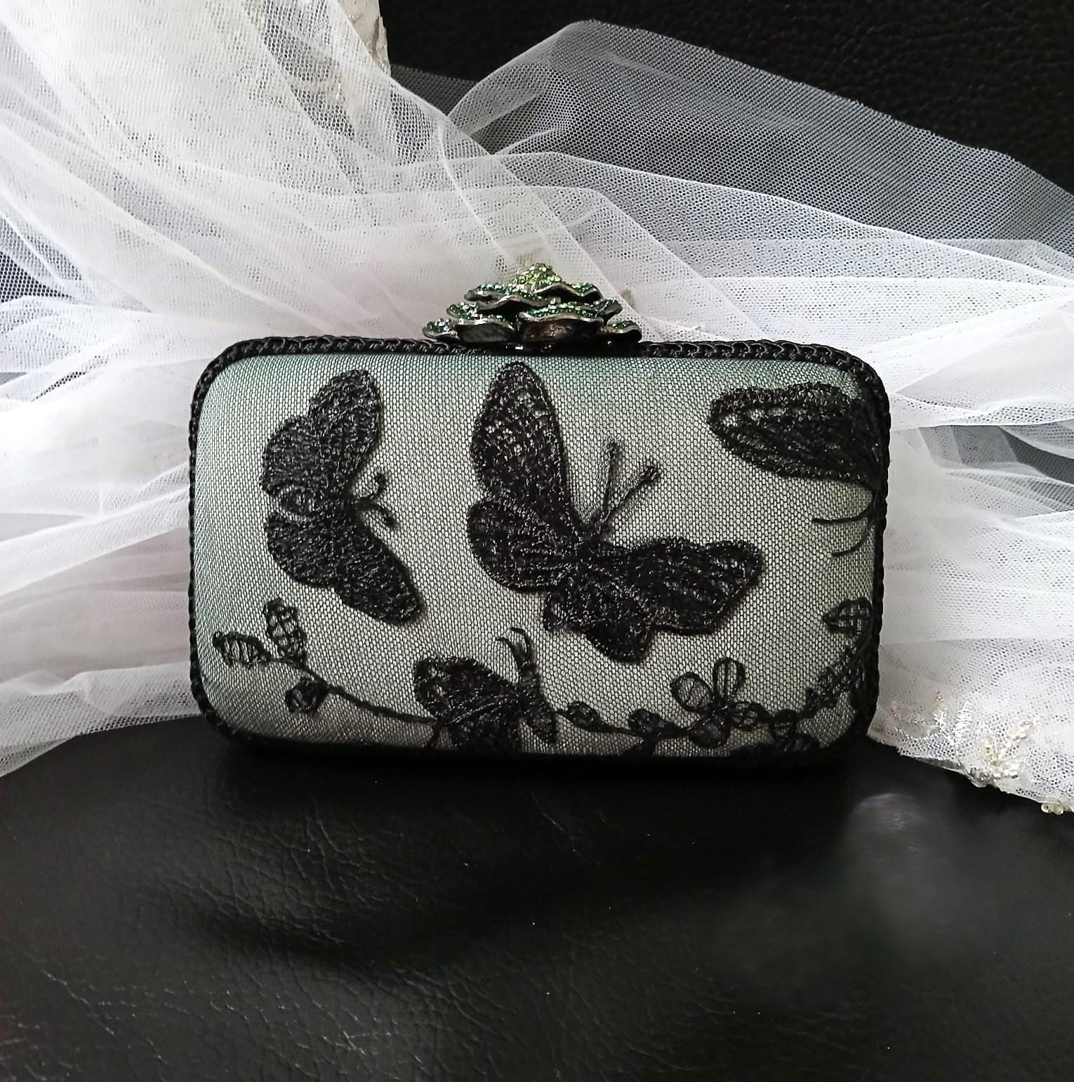 sage green with Black butterfly lace clutch bag on a dark surface with white fabric in the background