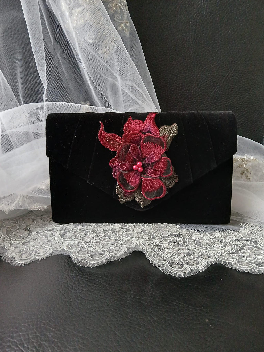 Black clutch with wine red floral embellishment on a lace surface