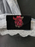 Black clutch with wine red floral embellishment on a lace surface