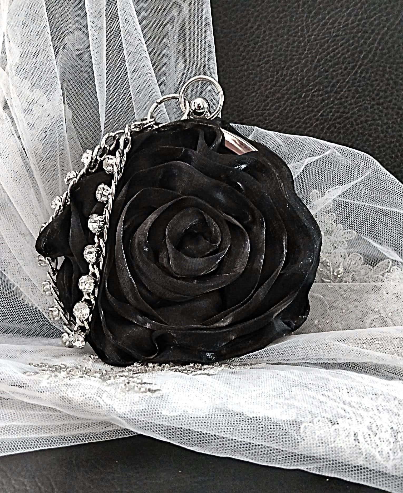 Black rose-shaped handbag with silver crystal chain on a white lace background
