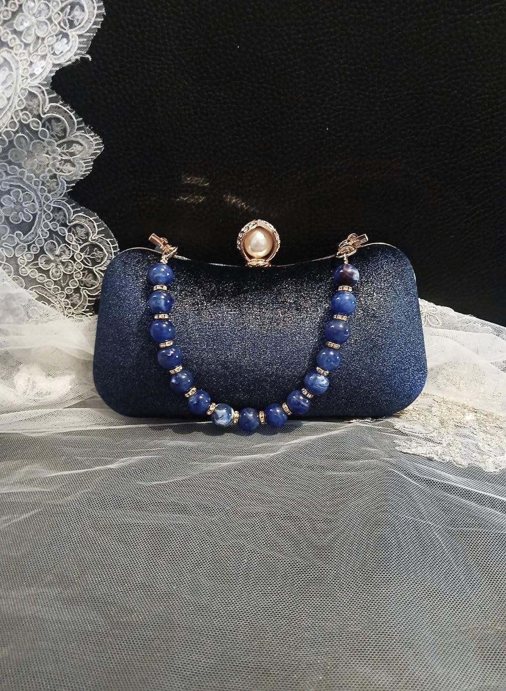 Blue clutch bag with beaded strap on a textured surface