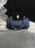 Blue clutch bag with beaded strap on a textured surface