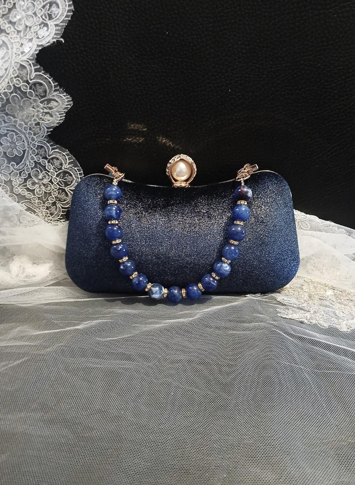 Blue clutch bag with beaded strap on a textured surface
