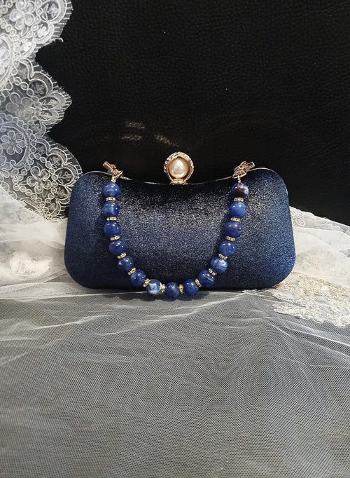 Blue clutch bag with beaded strap on a textured surface