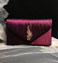 Dark Purple clutch bag with a decorative brooch on a textured surface