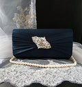 Navy blue clutch bag with decorative brooch and pearl handle on a lace fabric background