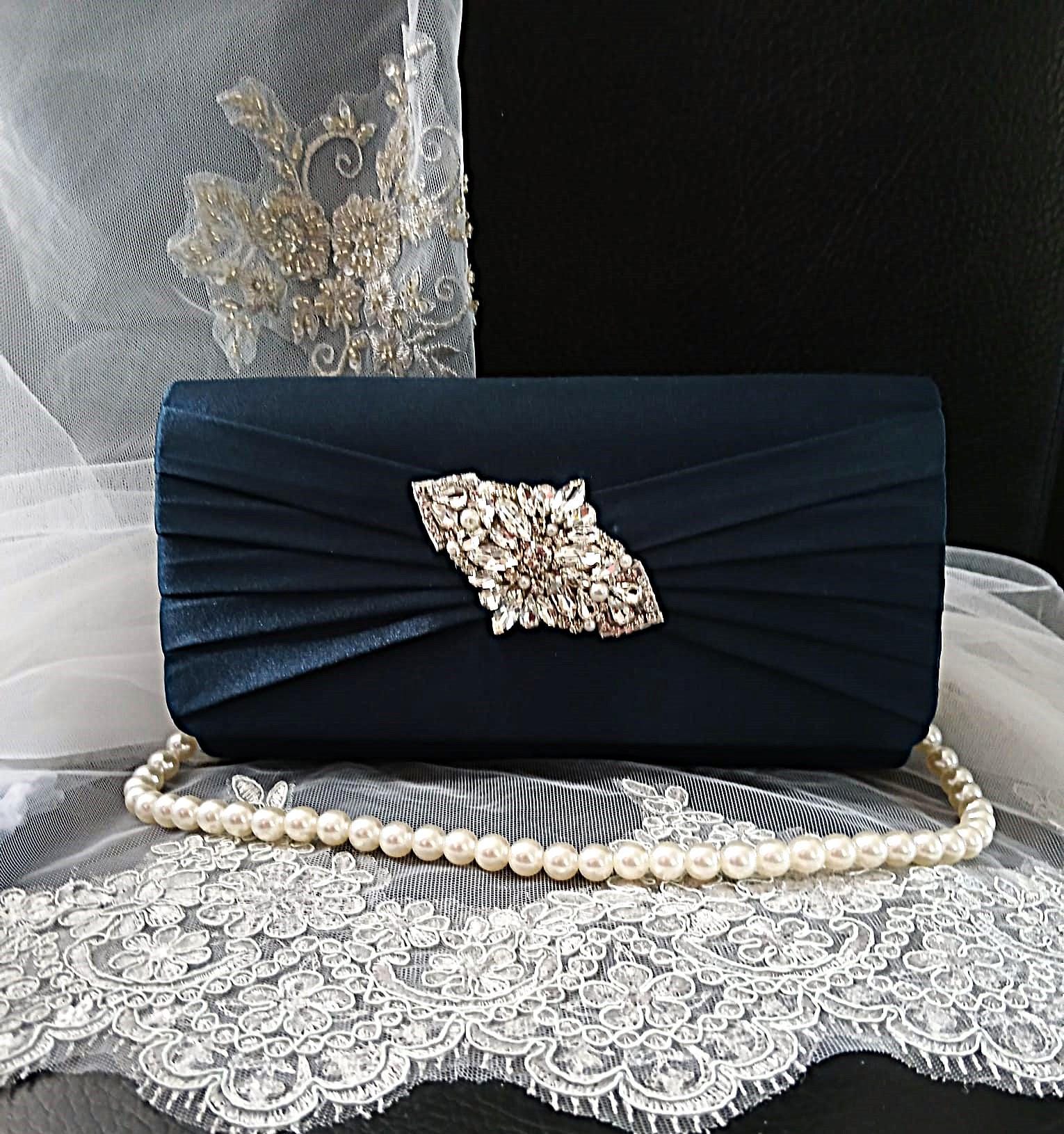 Navy blue clutch bag with decorative brooch and pearl handle on a lace fabric background
