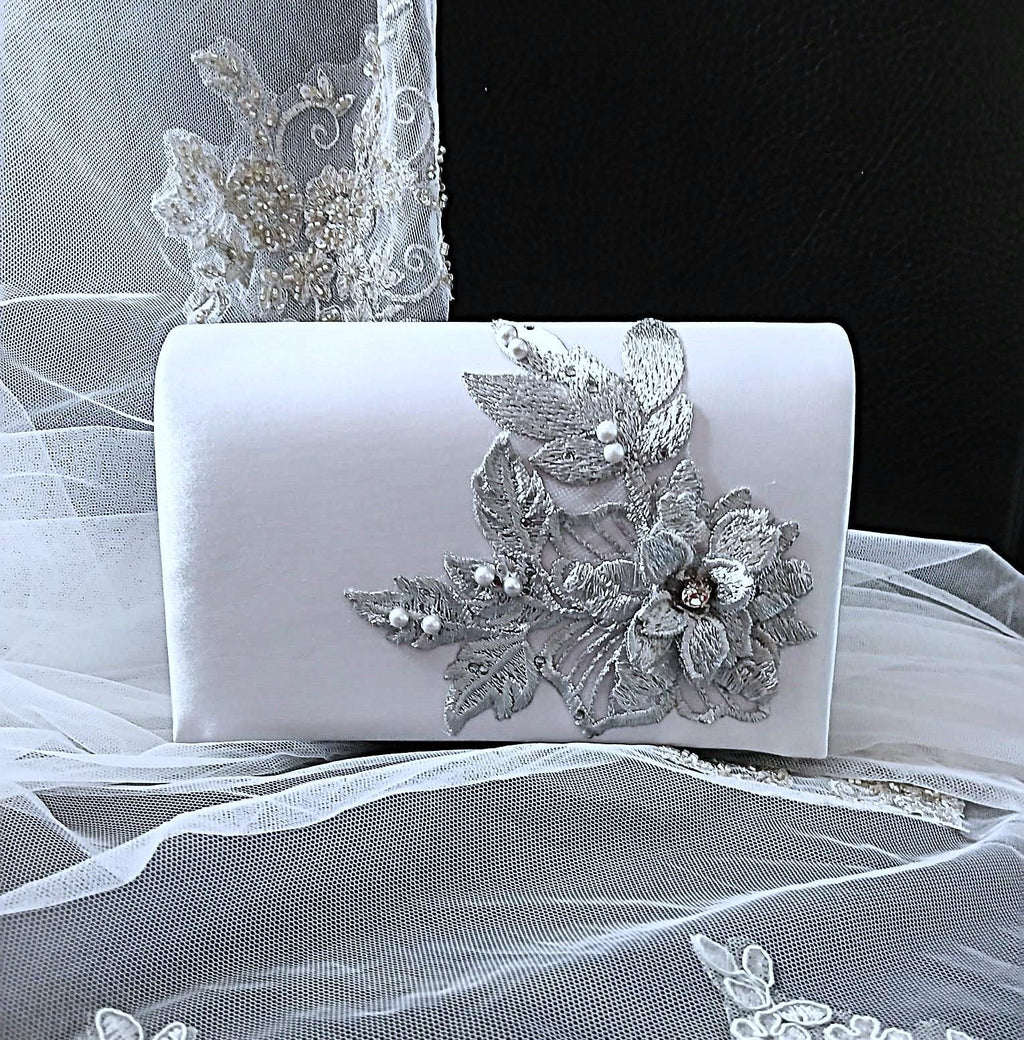 Silver clutch bag with floral embellishments on a white fabric background