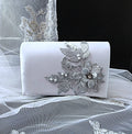 Silver clutch bag with floral embellishments on a white fabric background