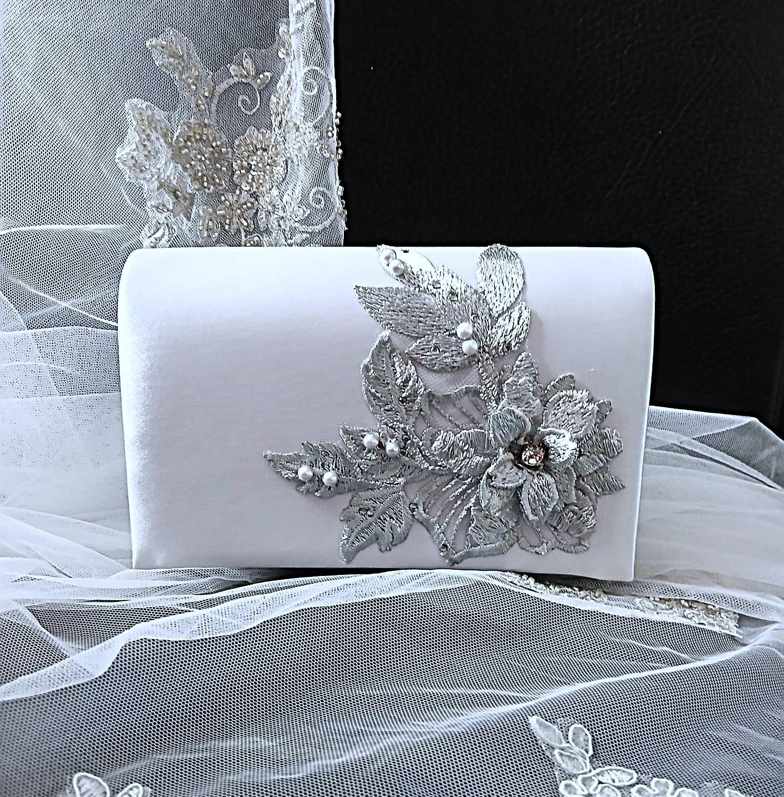 Silver clutch bag with floral embellishments on a white fabric background