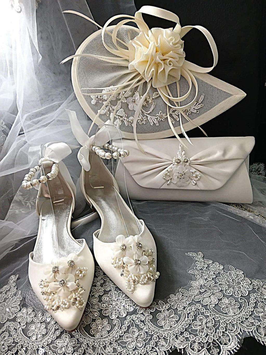 White wedding shoes with floral embellishments, matching hat, and clutch on a lace fabric background.