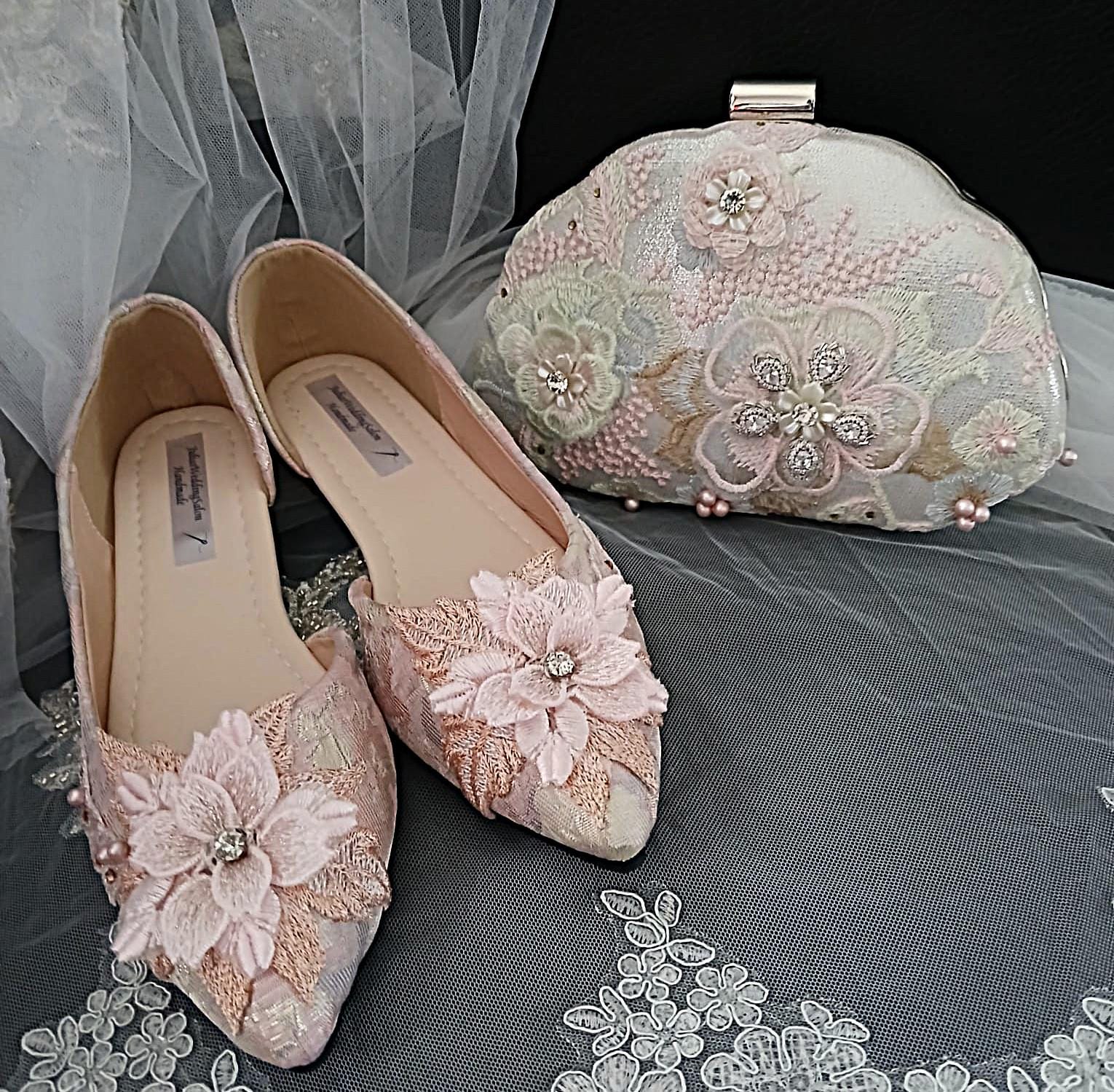 Pair of pink shoes with floral embellishments and a matching clutch bag on a gray fabric background.