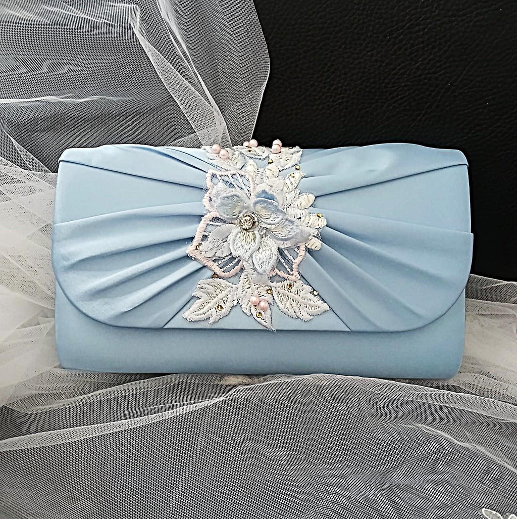 Light blue clutch bag with floral embellishment on a satin background