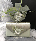 Sage green clutch bag and hat with floral embellishments on a black background