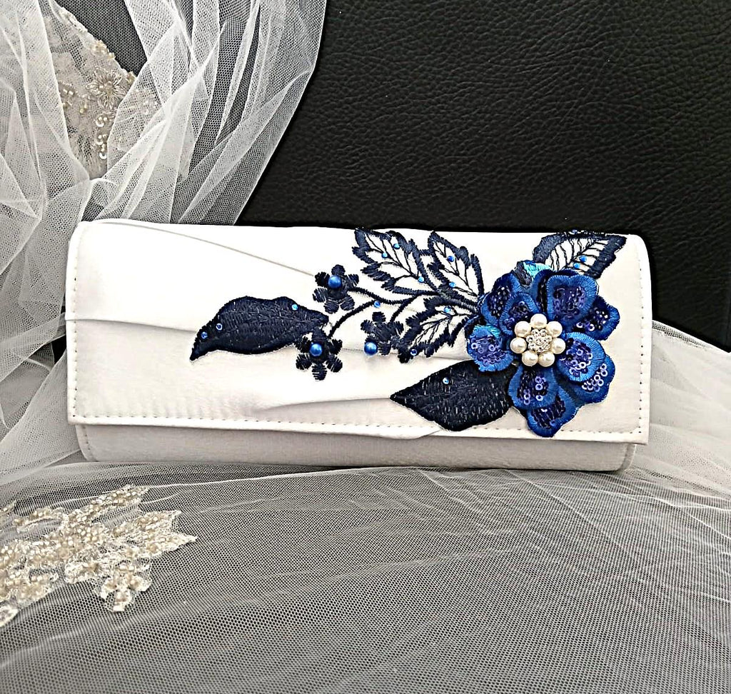 White clutch with blue floral embroidery on a black background