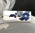 White clutch with blue floral embroidery on a black background