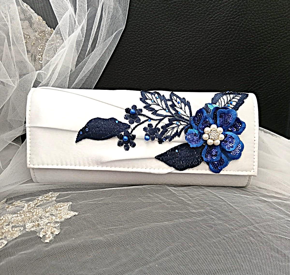 White clutch with blue floral embroidery on a black background