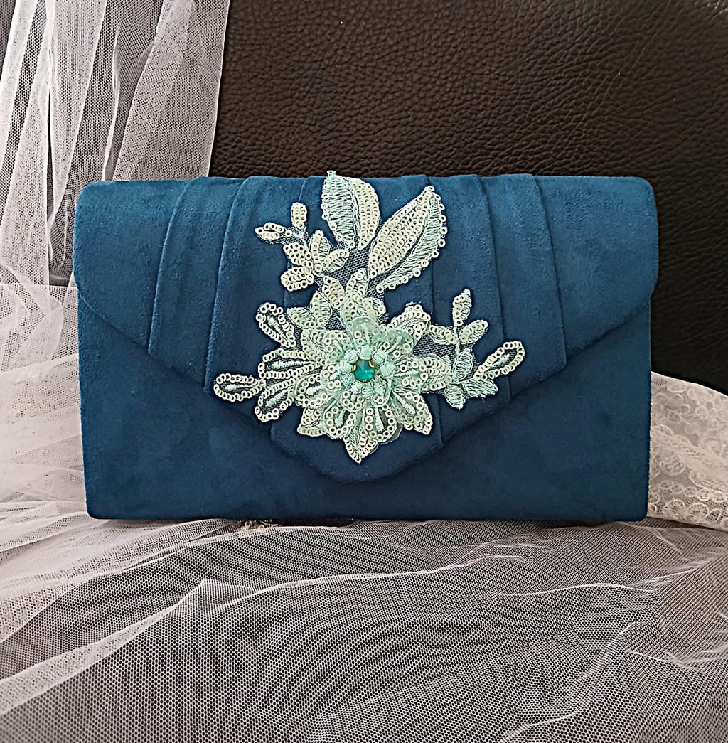 Peacock Blue clutch bag with floral embellishment on a textured surface