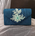Peacock Blue clutch bag with floral embellishment on a textured surface
