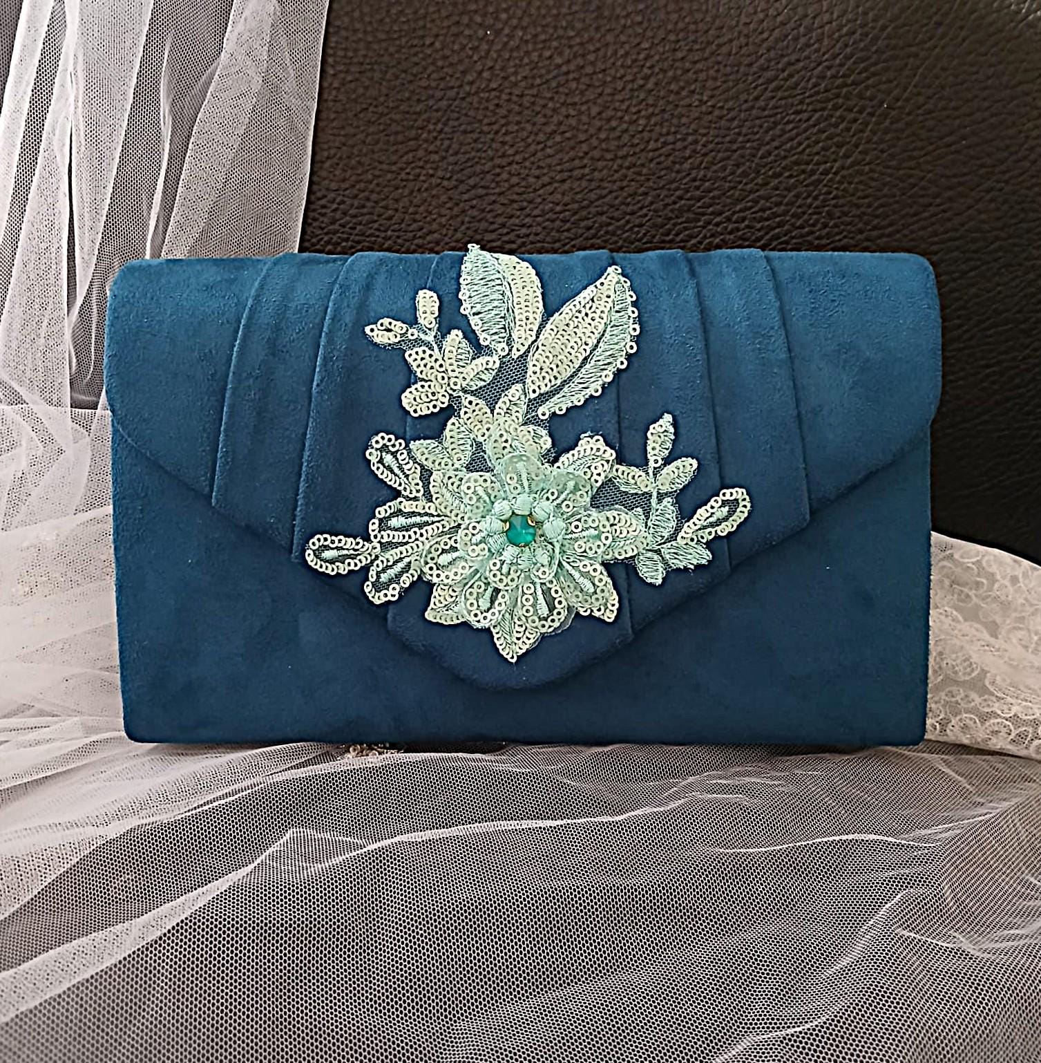 Peacock Blue clutch bag with floral embellishment on a textured surface