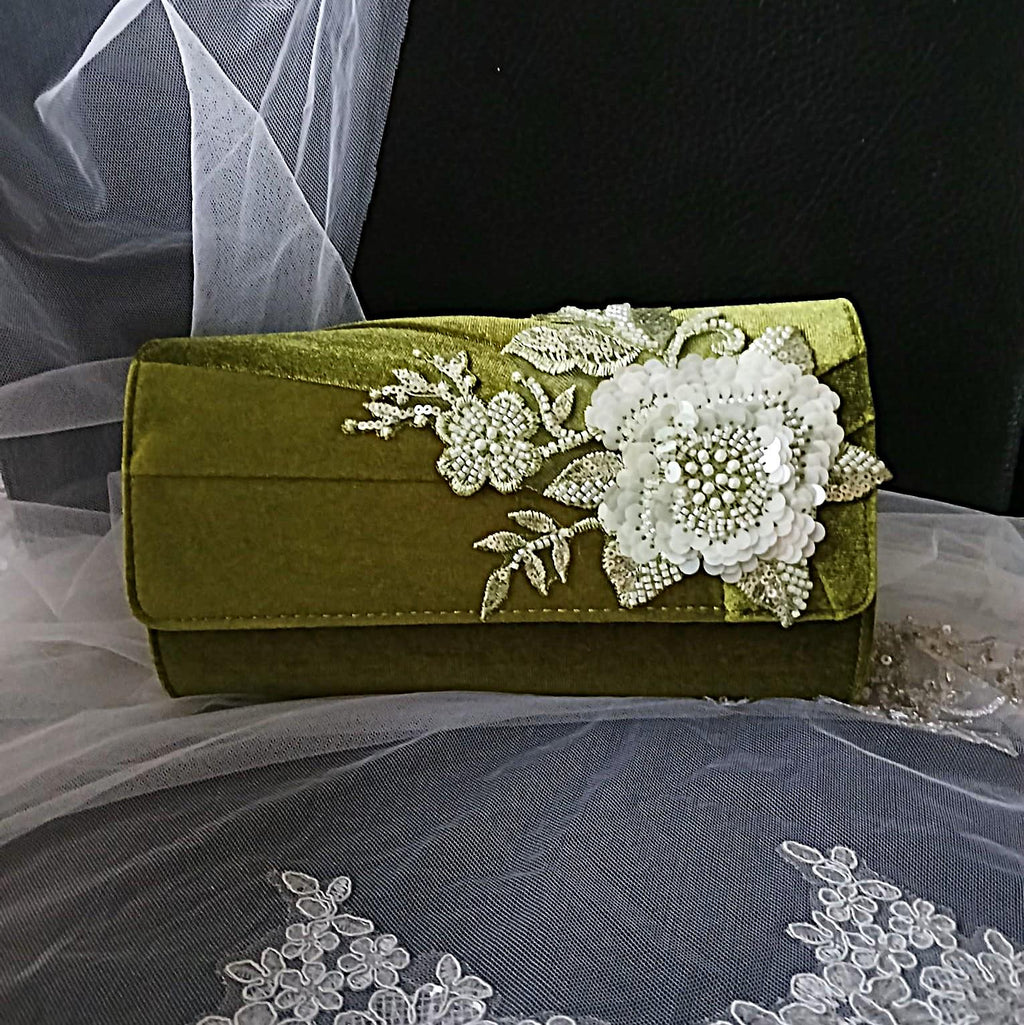 Olive Green clutch bag with floral embroidery on a fabric background