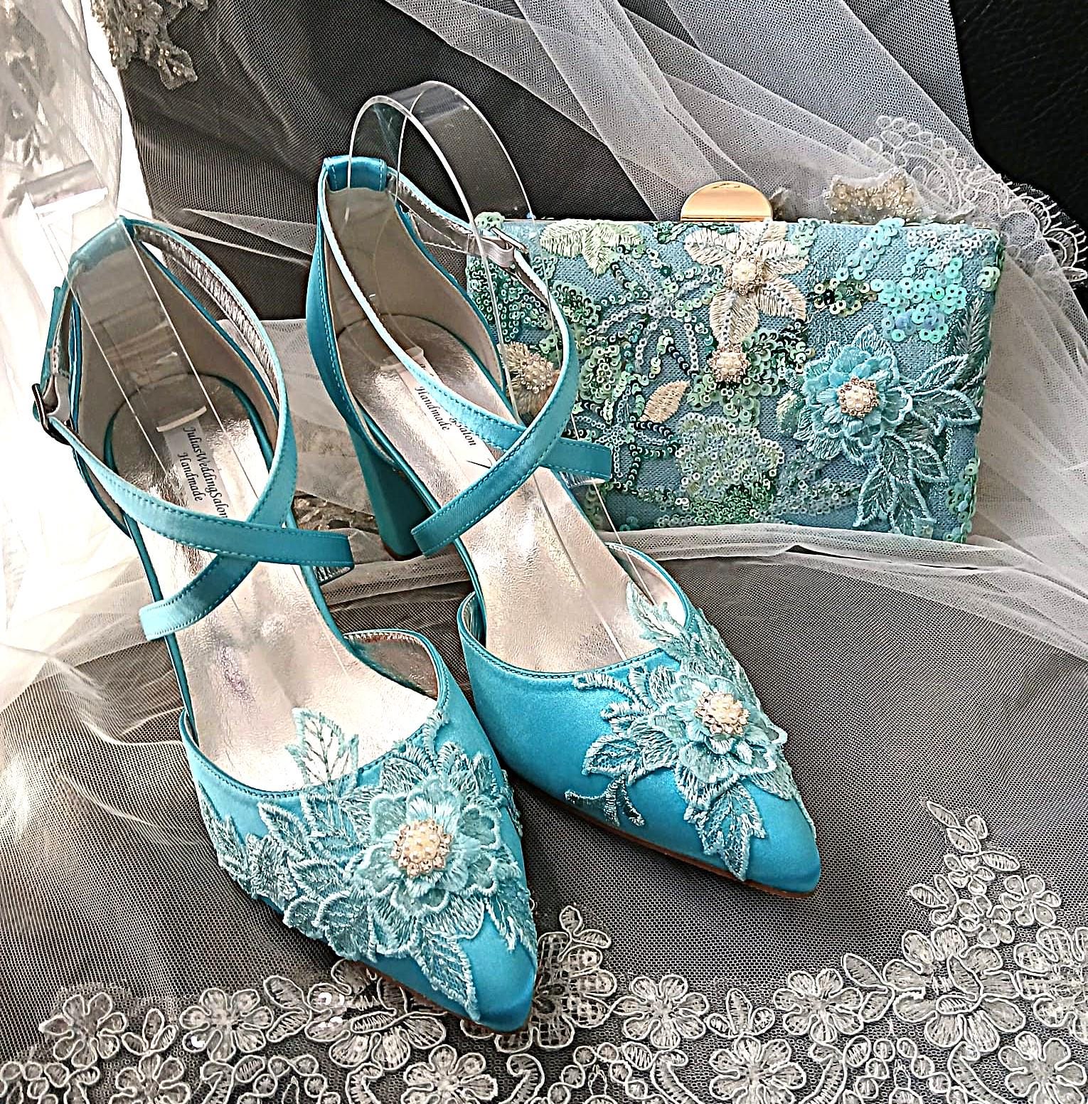 Set of turquoise wedding shoes and clutch with floral lace details on a gray fabric background.