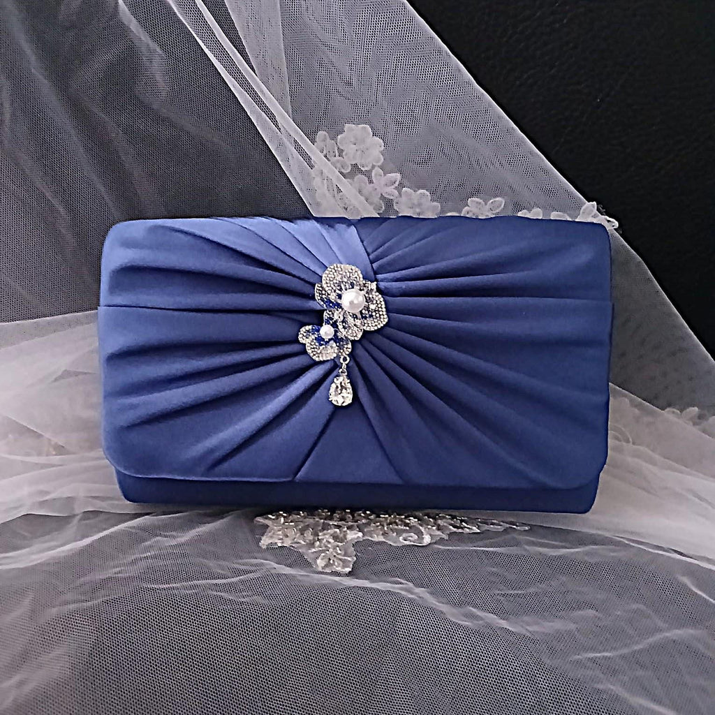 Blue clutch bag with decorative bow and pearl embellishment on a sheer fabric background
