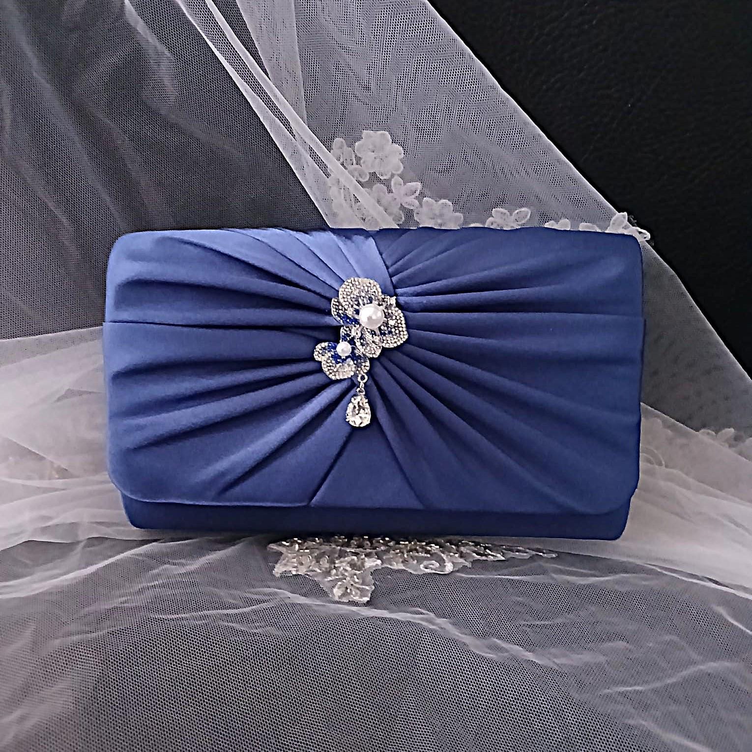 Blue clutch bag with decorative bow and pearl embellishment on a sheer fabric background