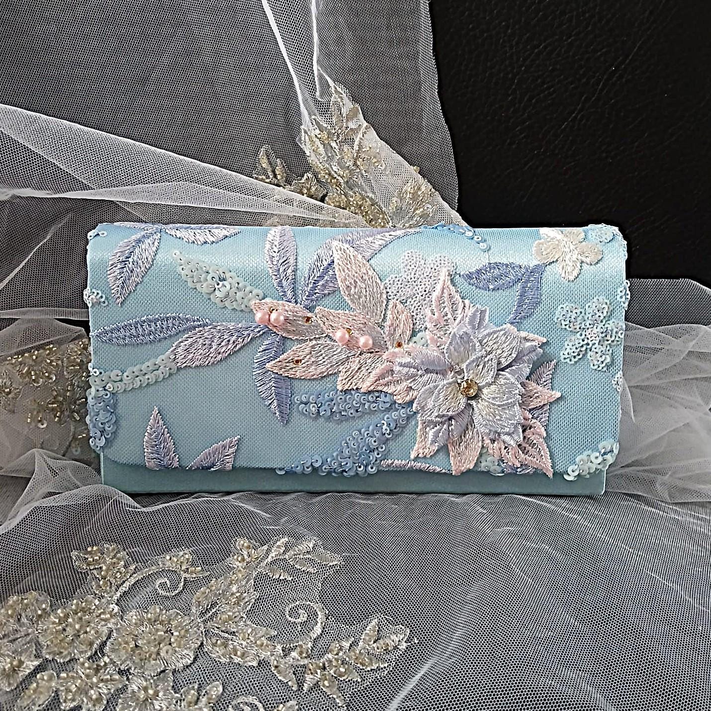 Light blue clutch bag with floral embroidery on a sheer fabric background