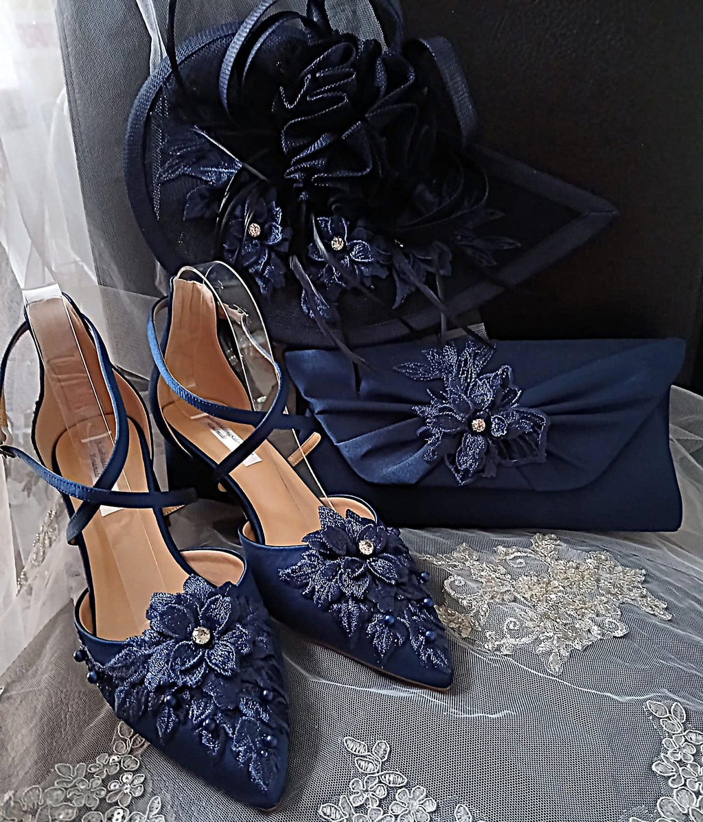 Navy blue shoes with floral embellishments and matching clutch and hat on a gray fabric background