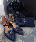 Navy blue shoes with floral embellishments and matching clutch and hat on a gray fabric background