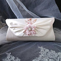 Ivory clutch bag with floral embellishment on a gray fabric background